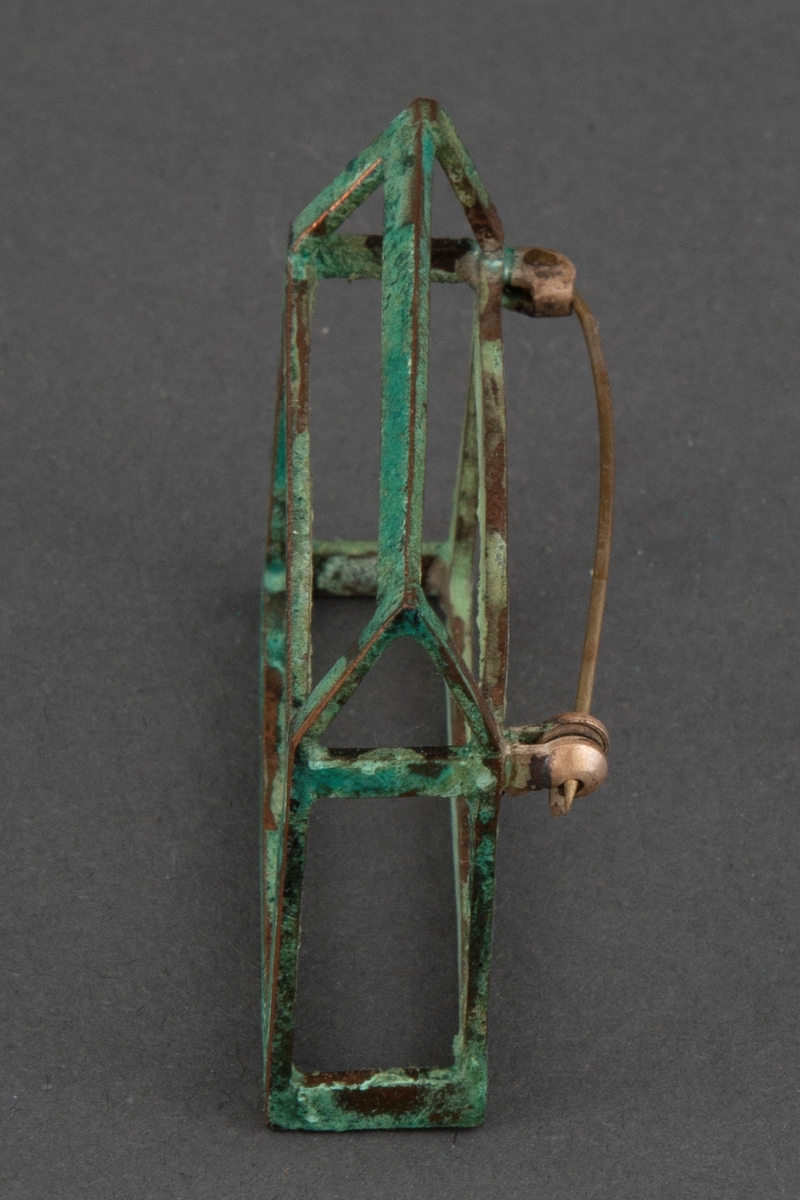 Brosje i patinert kobber. Brosjen har en arketypisk horisontal husform uten vegger.