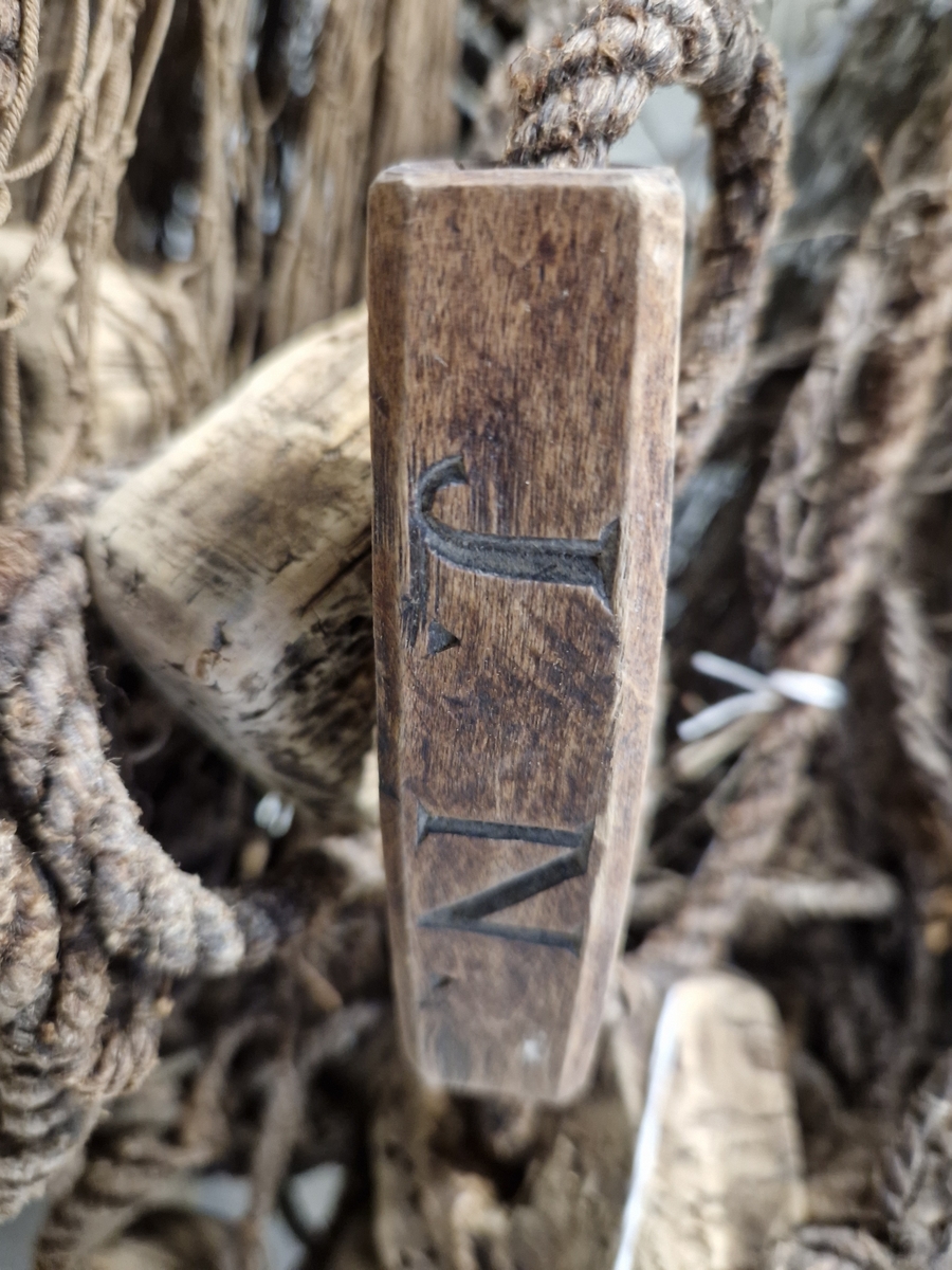 Lin og hampsnøre bunnet sammen til masker (garnlinet), påfestet korkebiter og gjennomhulete trebiter med innskåret bokstaver og tall
