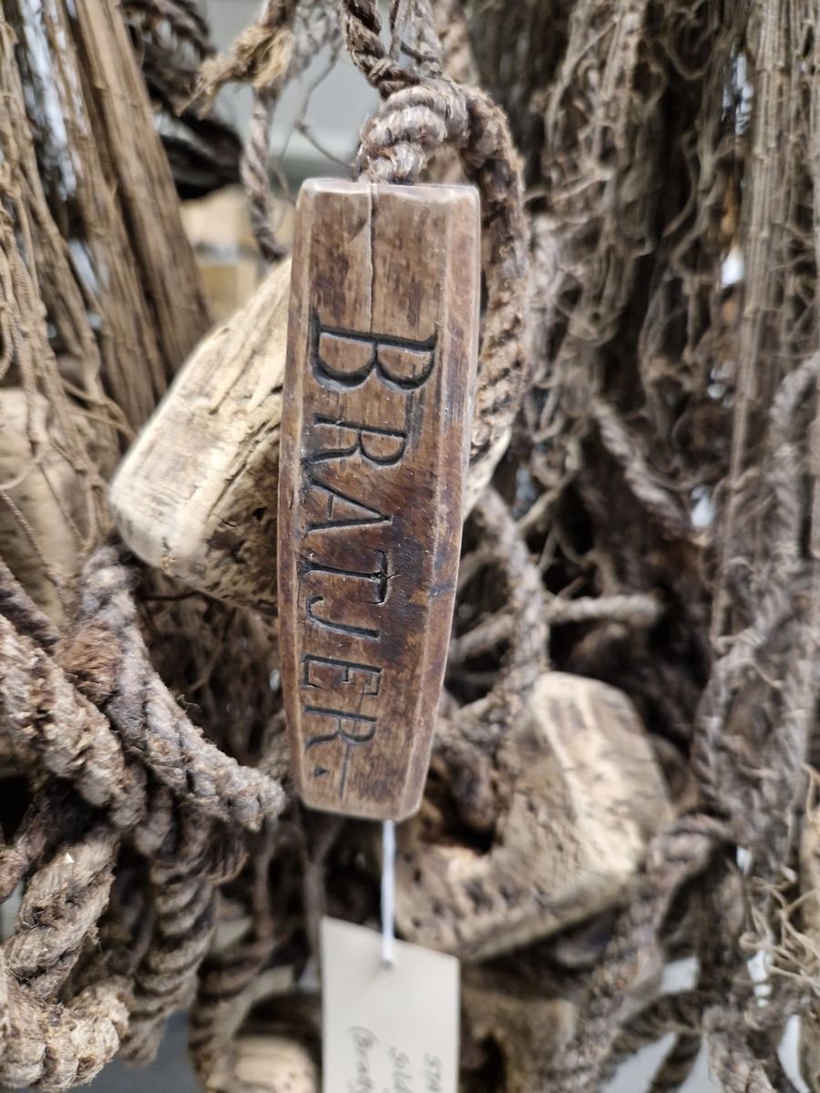 Lin og hampsnøre bunnet sammen til masker (garnlinet), påfestet korkebiter og gjennomhulete trebiter med innskåret bokstaver og tall
