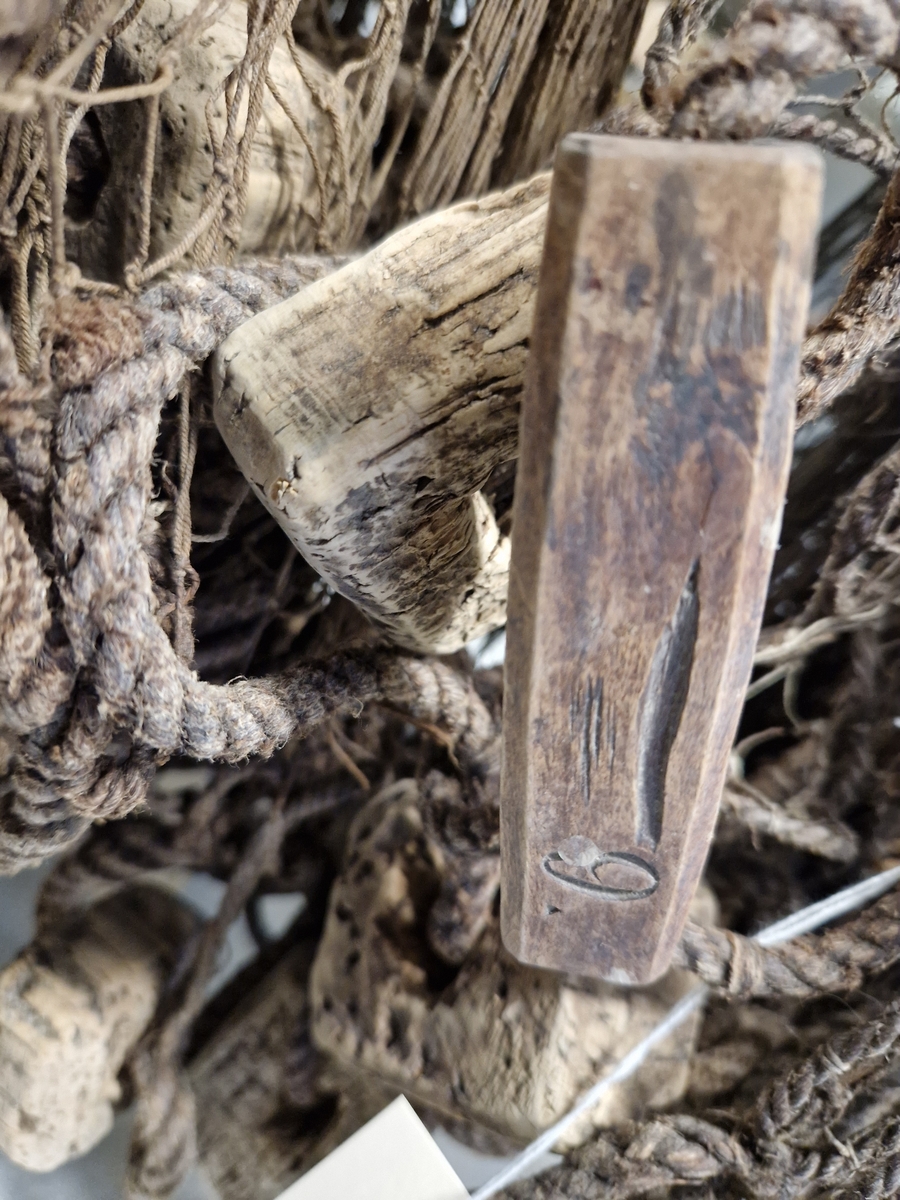 Lin og hampsnøre bunnet sammen til masker (garnlinet), påfestet korkebiter og gjennomhulete trebiter med innskåret bokstaver og tall
