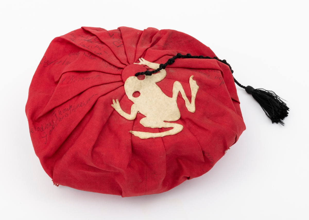 Rød russelue med slagord og autografer av blant annet jazzmusikerne Karin Krog og Jan Johansson m.f. påskrevet på lua. En hvit frosk i filt er limt på. Frosken er i følge giver Tone Marie Buberg logoen til Grorud høyere allmennskole.
Flere knuter i snora til dusken.