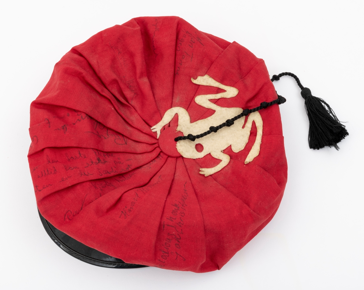 Rød russelue med slagord og autografer av blant annet jazzmusikerne Karin Krog og Jan Johansson m.f. påskrevet på lua. En hvit frosk i filt er limt på. Frosken er i følge giver Tone Marie Buberg logoen til Grorud høyere allmennskole.
Flere knuter i snora til dusken.