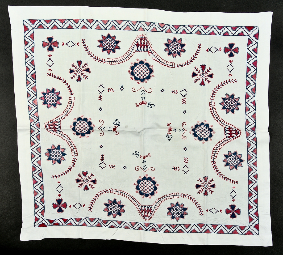 Vit linneduk med hallandsbroderi i färgerna blå och rosa. Broderiet är gjort i bomullstråd och har ett mönster som består av en board i zick-zack mönster och innanför boarden finns blommor. 

Bredd: 72 cm
Längs 69 cm