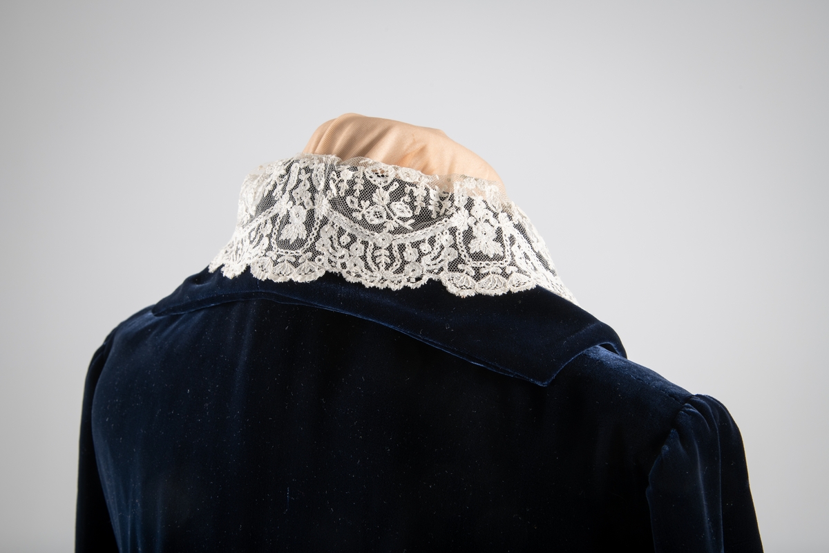 Den mørkeblå kjolen er datert til 1930-årene. Den ble sydd for Hedvig Sverdrup-Thygeson.
Det fortelles at kjolen er laget av den første viskosefløyelen produsert av cellulose fra trevirke som kom fra trevarebedriften Stangeskovene. Hedvig Sverdrup-Thygesons mann var aksjonær i Stangeskovene, og alle aksjonærkonene fikk noen meter av dette stoffet. Det er en sterk familiær tilknytning til Stangeskovene da selskapets grunnlegger, Nils Anker Stang, var Hedvigs morfar.
Ifølge etterkommere av kjolens første eier er kragen laget av italienske kniplinger.
