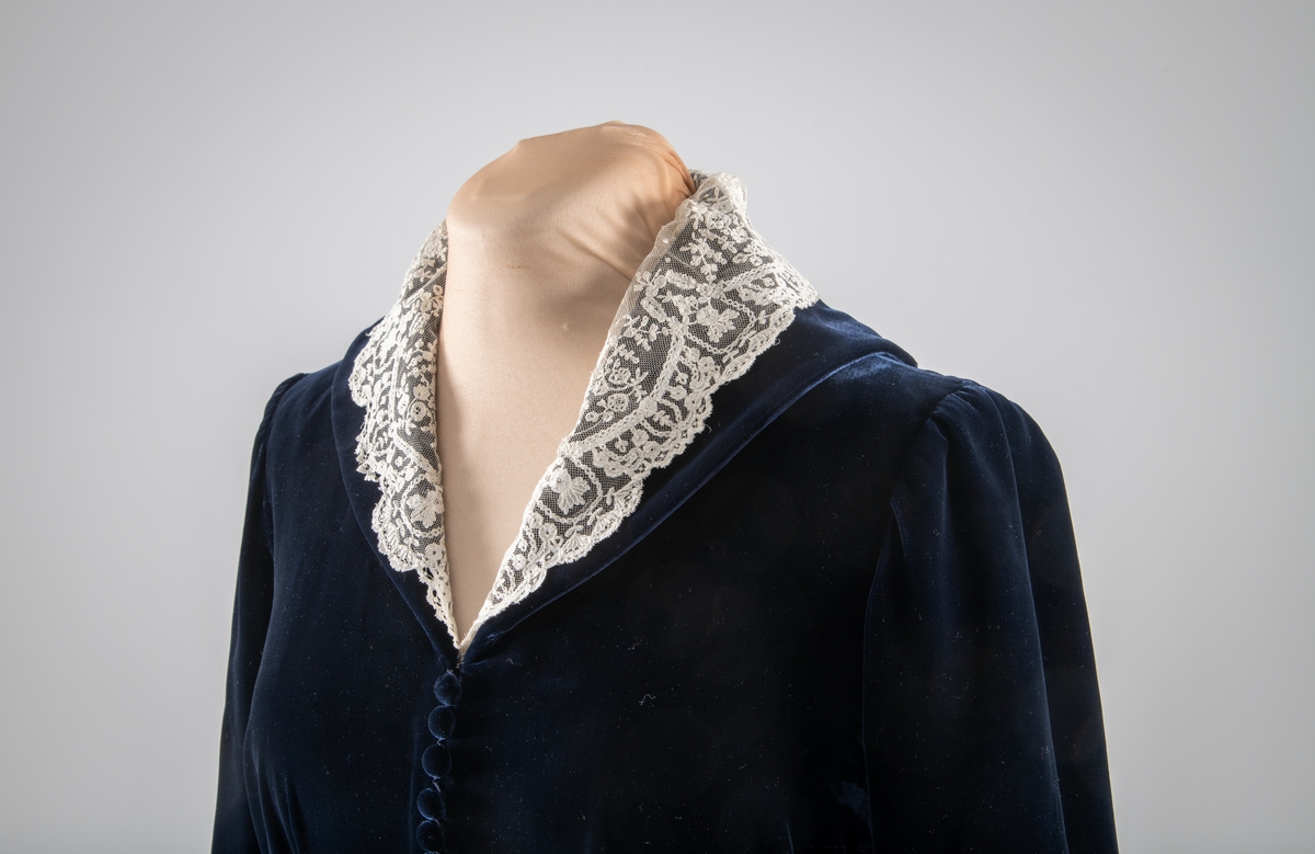 Den mørkeblå kjolen er datert til 1930-årene. Den ble sydd for Hedvig Sverdrup-Thygeson.
Det fortelles at kjolen er laget av den første viskosefløyelen produsert av cellulose fra trevirke som kom fra trevarebedriften Stangeskovene. Hedvig Sverdrup-Thygesons mann var aksjonær i Stangeskovene, og alle aksjonærkonene fikk noen meter av dette stoffet. Det er en sterk familiær tilknytning til Stangeskovene da selskapets grunnlegger, Nils Anker Stang, var Hedvigs morfar.
Ifølge etterkommere av kjolens første eier er kragen laget av italienske kniplinger.
