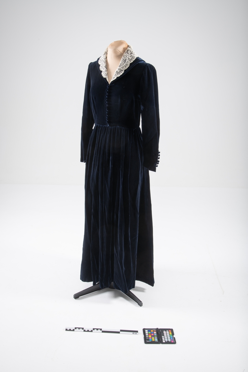 Den mørkeblå kjolen er datert til 1930-årene. Den ble sydd for Hedvig Sverdrup-Thygeson.
Det fortelles at kjolen er laget av den første viskosefløyelen produsert av cellulose fra trevirke som kom fra trevarebedriften Stangeskovene. Hedvig Sverdrup-Thygesons mann var aksjonær i Stangeskovene, og alle aksjonærkonene fikk noen meter av dette stoffet. Det er en sterk familiær tilknytning til Stangeskovene da selskapets grunnlegger, Nils Anker Stang, var Hedvigs morfar.
Ifølge etterkommere av kjolens første eier er kragen laget av italienske kniplinger.
