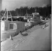 Två båtar står i en hamn. De är täckta med snö och det hänger istappar från relingarna.