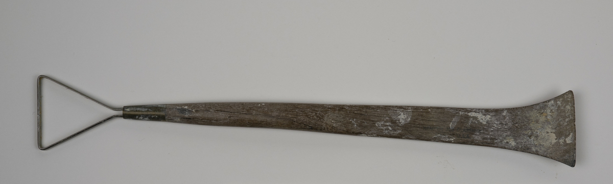 Modellerslynge brukt av Nils Aas. Slyngen består av et flatt metallbånd festet i enden av et trehåndtak. Motsatt ende av håndtaket er formet som en spatel. Det er noe rester etter gips.