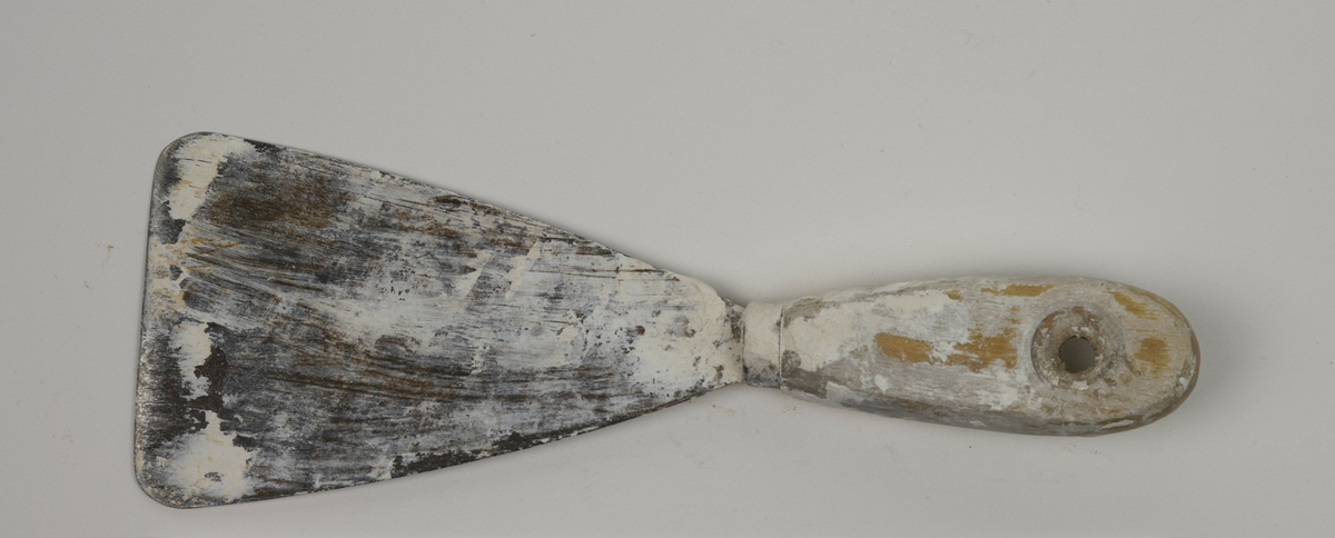 Spatel brukt av Nils Aas til modellering. Den består av et stykke metall formet til en flat trekantform i enden av et trehåndtak. Hele verktøyet er fullt av rester etter gips og leire. 