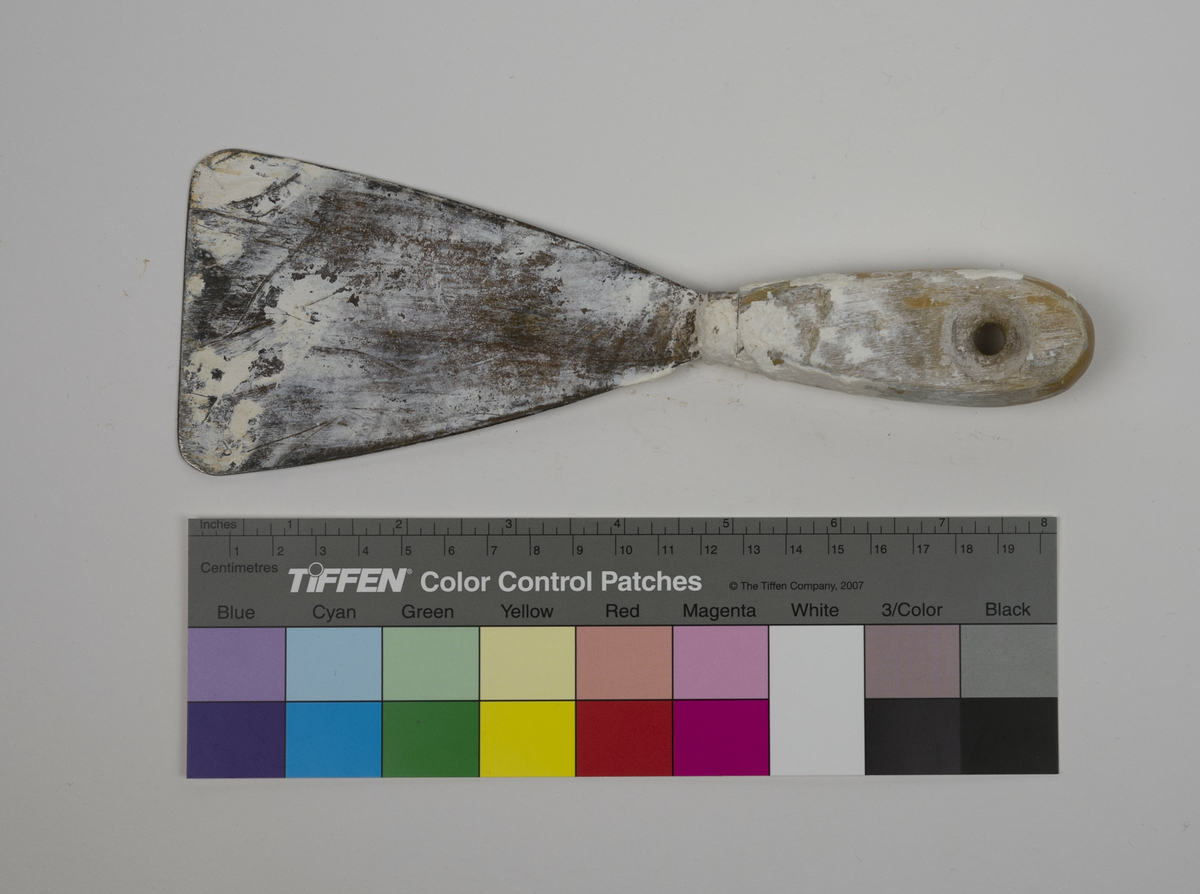 Spatel brukt av Nils Aas til modellering. Den består av et stykke metall formet til en flat trekantform i enden av et trehåndtak. Hele verktøyet er fullt av rester etter gips og leire. 