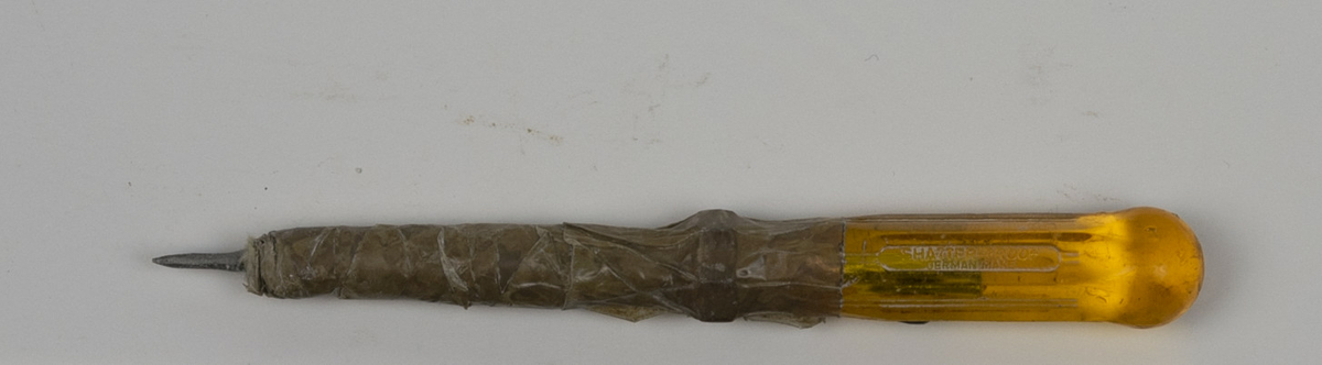 Syl brukt av Nils Aas til modellering. Håndtaket er av gul plast. Sylen er tilsynelatende hjemmelaget av et skrujern og en spiker festet sammen med brun teip.