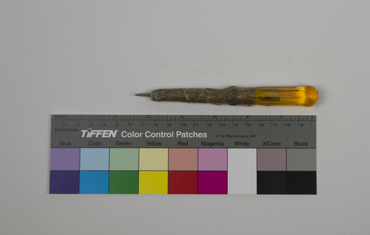 Syl brukt av Nils Aas til modellering. Håndtaket er av gul plast. Sylen er tilsynelatende hjemmelaget av et skrujern og en spiker festet sammen med brun teip.