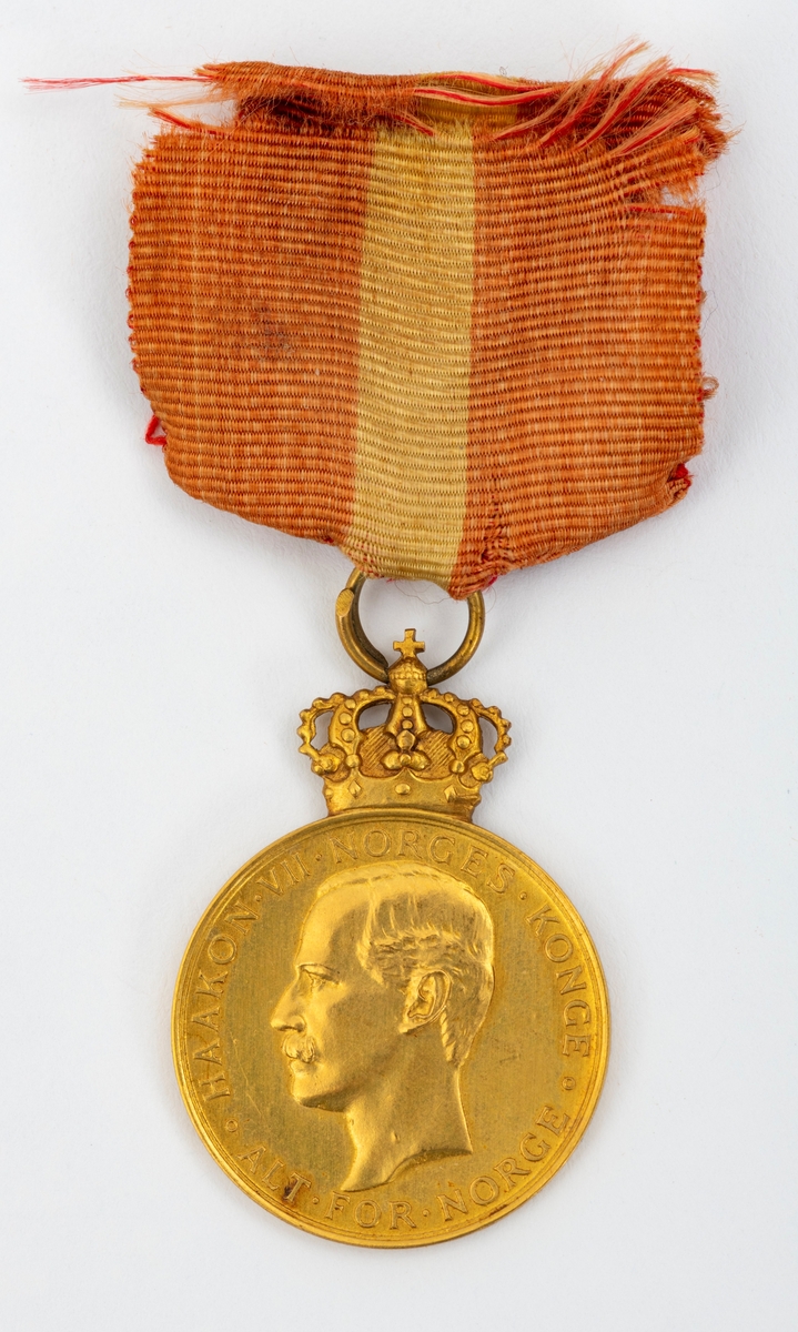 Kongens fortjenstmedalje i gull, med bånd i rødt med gul stripe i midten; alt festet til ramme av tre. På forsiden av medaljen er et portrett av Kong Haakon, omkranset av teksten "Haakon VII Norges Konge. Alt for Norge."