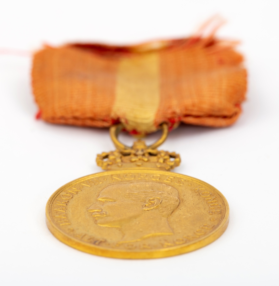 Kongens fortjenstmedalje i gull, med bånd i rødt med gul stripe i midten; alt festet til ramme av tre. På forsiden av medaljen er et portrett av Kong Haakon, omkranset av teksten "Haakon VII Norges Konge. Alt for Norge."
