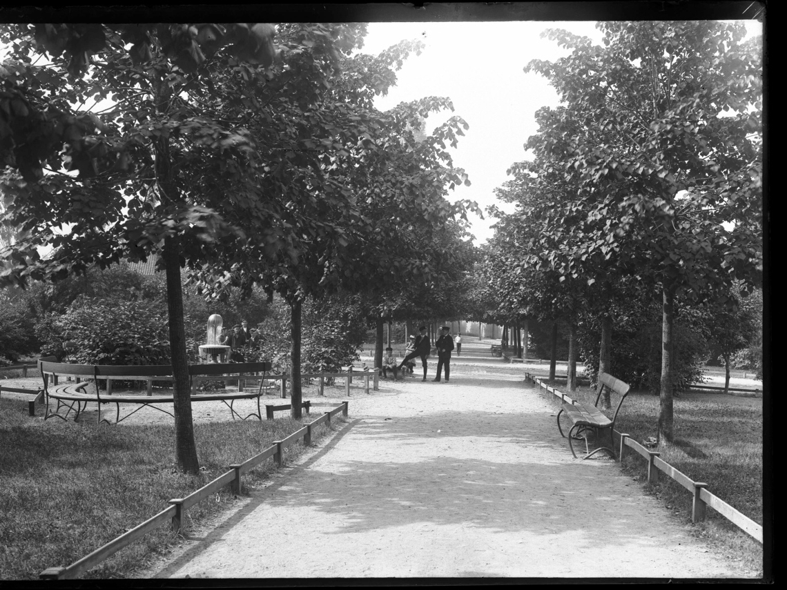 En park med trær, busker, fontene, benker, barn og unge.