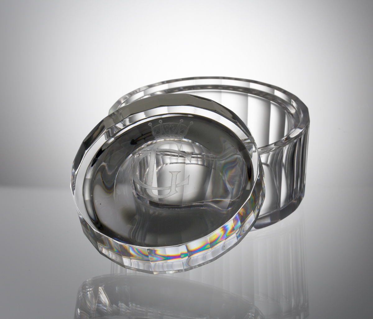 Formgivare: Sven Palmqvist. Cylindrisk låg skål med lock. Stående fasetter. På locket ett graverat kungligt monogram: "CG"* 
samt en kungakrona. 

* "CG" - Carl XVI Gustaf 1946-     (reg. 1973-      ).