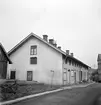 Svunnen vy utmed Gästgivaregatan i Mjölby. Gatans sträckning genom kvarteret kom att läggas igen när ny bebyggelse uppfördes från 1970-talet. Fotoåret 1950 och ännu en tid låg denna affärsbyggnad i hörnet mot Kungsvägen. I fonden skymtar Kanikegården.