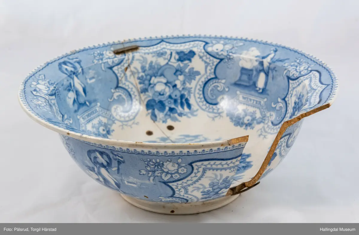 Flint? Hvitt, rundt, fotring. Utbuket side. markert kant med blå dekorasjoner. I bunnen landskap med jeger, symboliserende "april". Veggen innv. og utv. - blomsterklaser omgitt av knekkete bånd, mellom dem kvinnefigurer. Sprukket og klinket. Et stykke mangler. Bunnen stemplet: "Patterson" 12.

R.B.S.