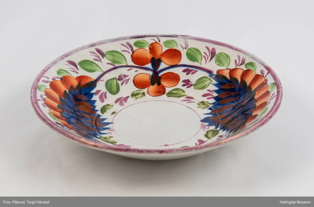 a) Kopp: Stentøy, hvit, liten. Markert fotring. Siden svunget. Utv. polygongal, dekorert med 2 store trekantede blomster i blått og rødt. Mellom dem 6 røde og grønne blad.
b) Skål: Stentøy, hvt, rund. Forholdsvis dyp med skrå side. Samme dekor som koppen. R.B.S.