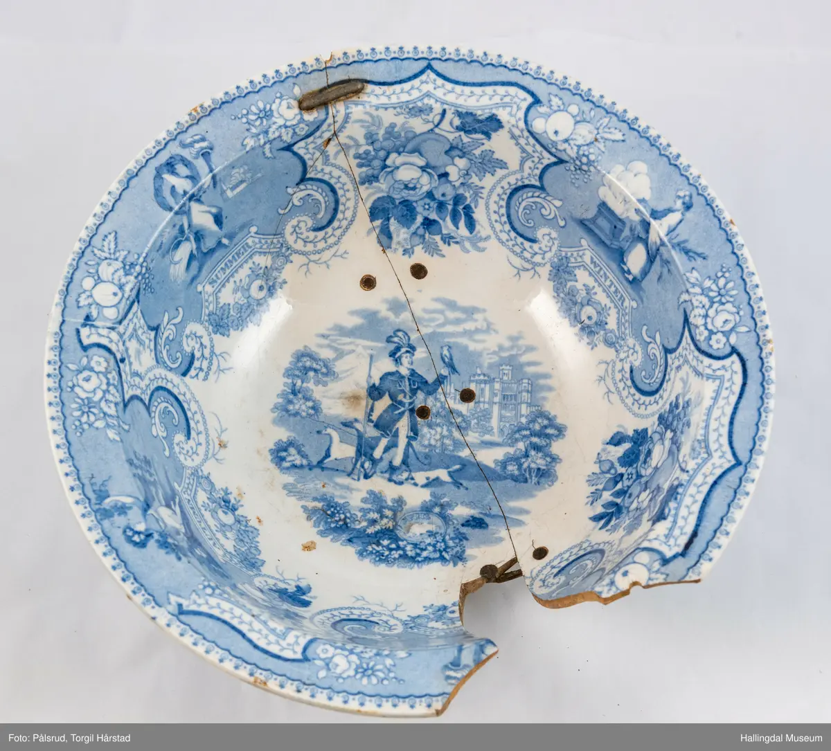 Flint? Hvitt, rundt, fotring. Utbuket side. markert kant med blå dekorasjoner. I bunnen landskap med jeger, symboliserende "april". Veggen innv. og utv. - blomsterklaser omgitt av knekkete bånd, mellom dem kvinnefigurer. Sprukket og klinket. Et stykke mangler. Bunnen stemplet: "Patterson" 12.

R.B.S.