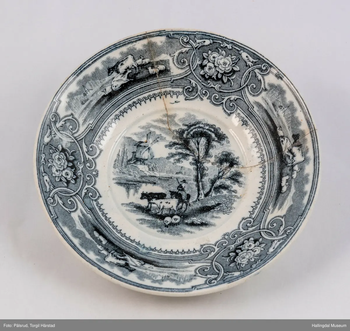 a) Kopp: Stentøy, hvit, liten. Markert fotring. Siden svunget. Utv. polygongal, trykte sorte dekorasjoner. I bunnen innv. landskap. langs randen innv. og utv. 2 blomsterornamenter og 2 felt med kuer og sauer i et slettelandskap. Sprukket.
b) Skål: Stentøy, hvt, rund. Forholdsvis dyp med skrå side. Siden samme dekor som koppen. I bunnen landskap med trær, vindmølle, rytter og kyr. Sprukket og limt. R.B.S.