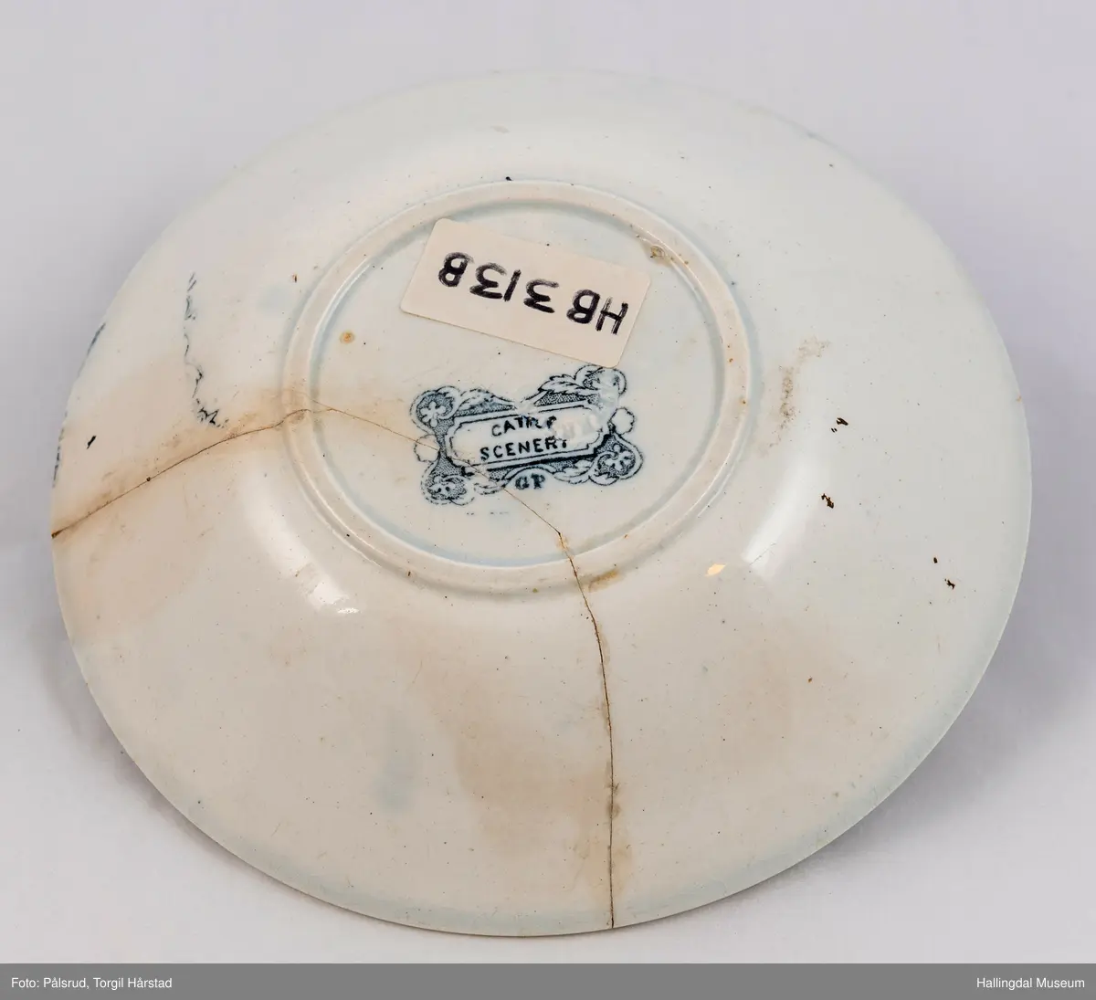 a) Kopp: Stentøy, hvit, liten. Markert fotring. Siden svunget. Utv. polygongal, trykte sorte dekorasjoner. I bunnen innv. landskap. langs randen innv. og utv. 2 blomsterornamenter og 2 felt med kuer og sauer i et slettelandskap. Sprukket.
b) Skål: Stentøy, hvt, rund. Forholdsvis dyp med skrå side. Siden samme dekor som koppen. I bunnen landskap med trær, vindmølle, rytter og kyr. Sprukket og limt. R.B.S.