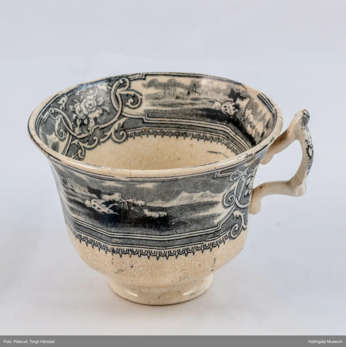 a) Kopp: Stentøy, hvit, liten. Markert fotring. Siden svunget. Utv. polygongal, trykte sorte dekorasjoner. I bunnen innv. landskap. langs randen innv. og utv. 2 blomsterornamenter og 2 felt med kuer og sauer i et slettelandskap. Sprukket.
b) Skål: Stentøy, hvt, rund. Forholdsvis dyp med skrå side. Siden samme dekor som koppen. I bunnen landskap med trær, vindmølle, rytter og kyr. Sprukket og limt. R.B.S.