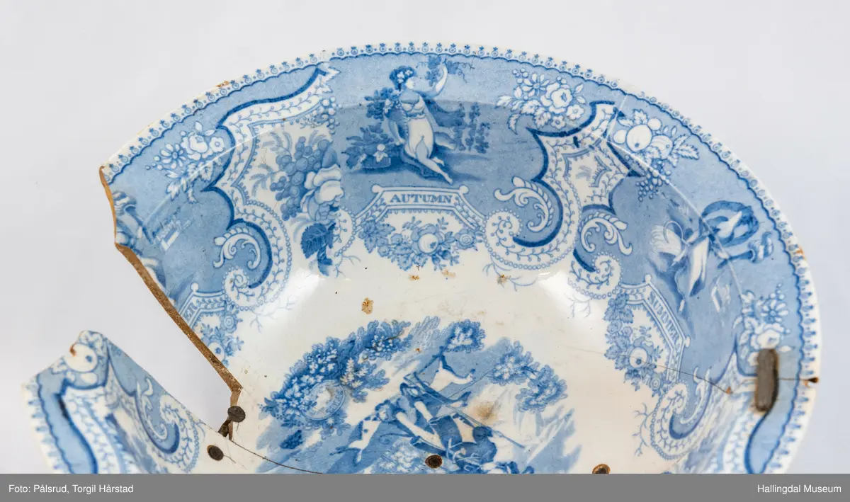 Flint? Hvitt, rundt, fotring. Utbuket side. markert kant med blå dekorasjoner. I bunnen landskap med jeger, symboliserende "april". Veggen innv. og utv. - blomsterklaser omgitt av knekkete bånd, mellom dem kvinnefigurer. Sprukket og klinket. Et stykke mangler. Bunnen stemplet: "Patterson" 12.

R.B.S.