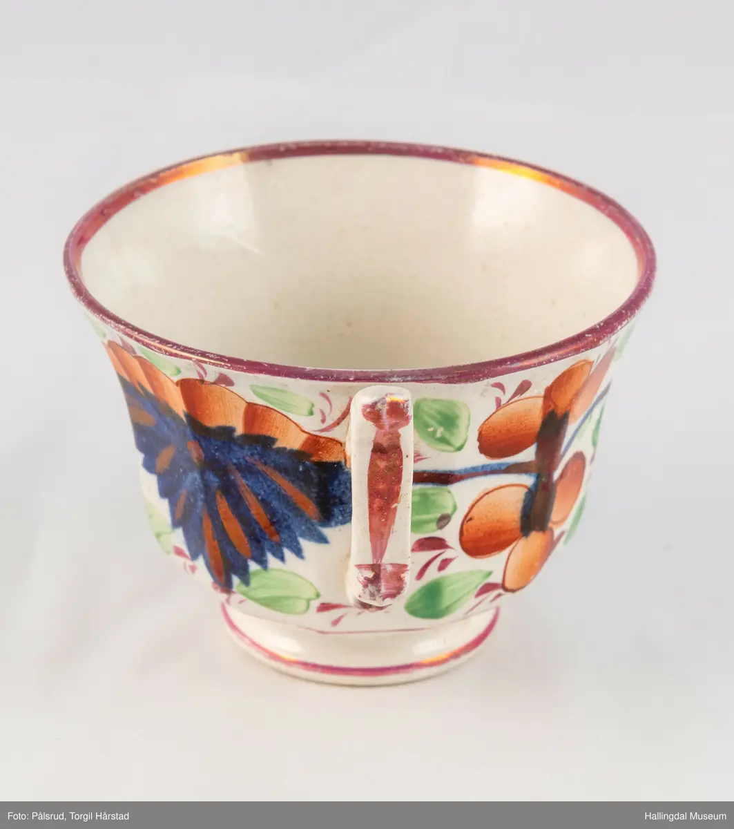 a) Kopp: Stentøy, hvit, liten. Markert fotring. Siden svunget. Utv. polygongal, dekorert med 2 store trekantede blomster i blått og rødt. Mellom dem 6 røde og grønne blad.
b) Skål: Stentøy, hvt, rund. Forholdsvis dyp med skrå side. Samme dekor som koppen. R.B.S.