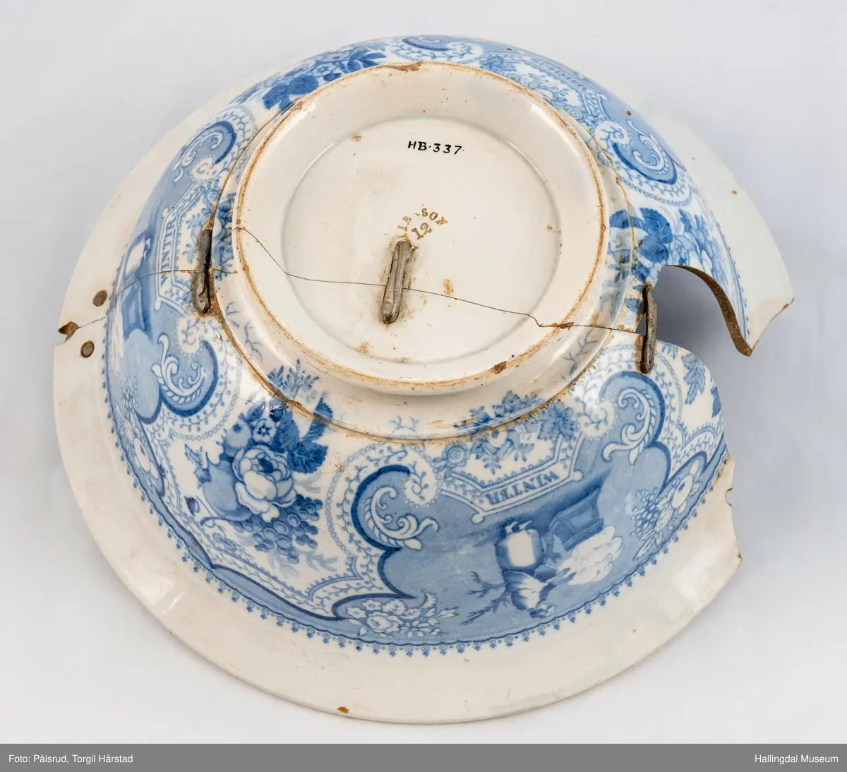 Flint? Hvitt, rundt, fotring. Utbuket side. markert kant med blå dekorasjoner. I bunnen landskap med jeger, symboliserende "april". Veggen innv. og utv. - blomsterklaser omgitt av knekkete bånd, mellom dem kvinnefigurer. Sprukket og klinket. Et stykke mangler. Bunnen stemplet: "Patterson" 12.

R.B.S.