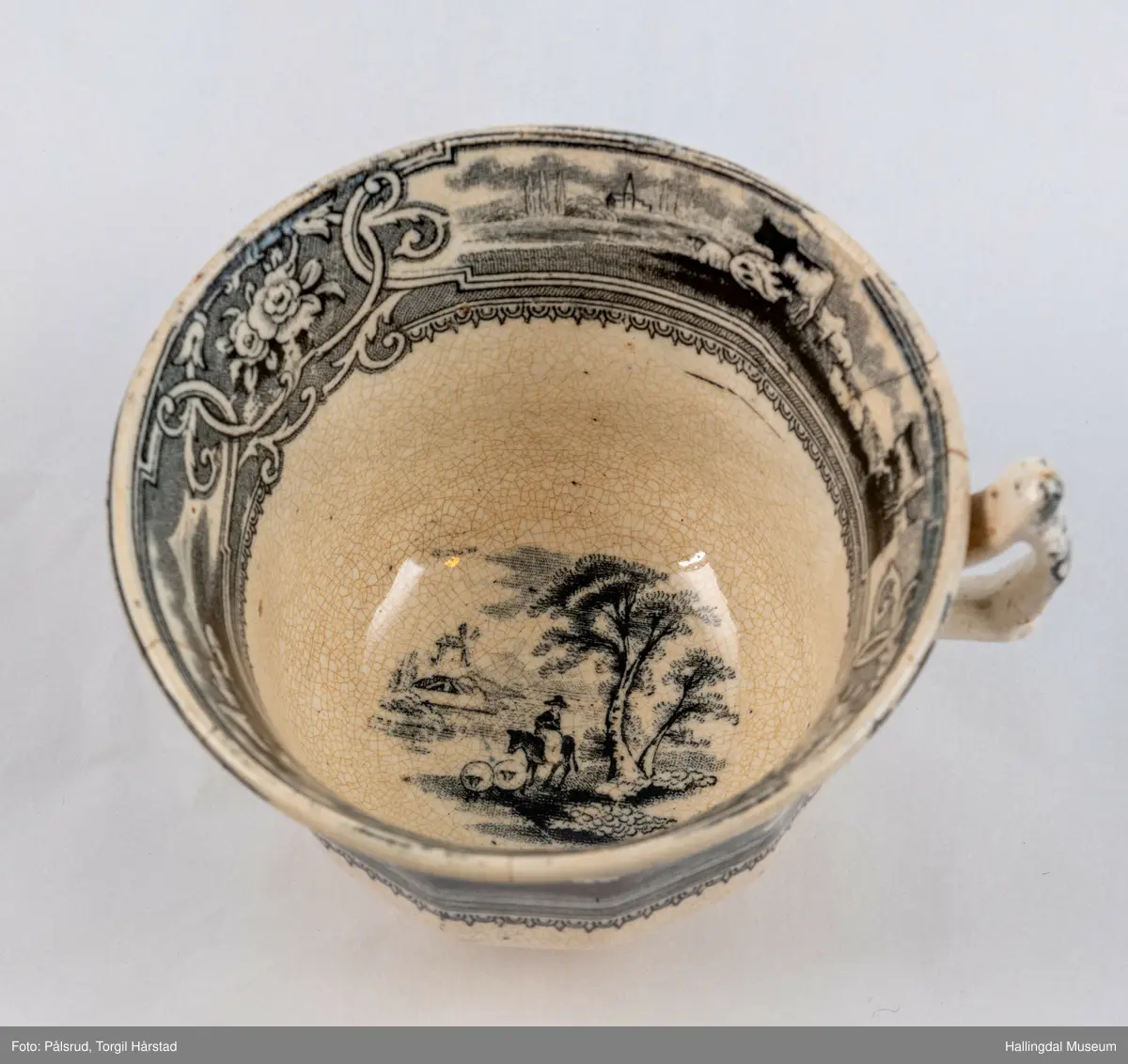 a) Kopp: Stentøy, hvit, liten. Markert fotring. Siden svunget. Utv. polygongal, trykte sorte dekorasjoner. I bunnen innv. landskap. langs randen innv. og utv. 2 blomsterornamenter og 2 felt med kuer og sauer i et slettelandskap. Sprukket.
b) Skål: Stentøy, hvt, rund. Forholdsvis dyp med skrå side. Siden samme dekor som koppen. I bunnen landskap med trær, vindmølle, rytter og kyr. Sprukket og limt. R.B.S.