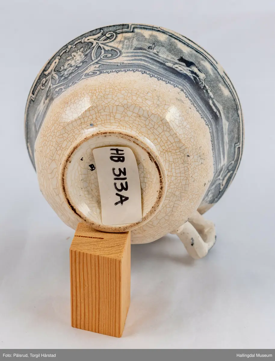 a) Kopp: Stentøy, hvit, liten. Markert fotring. Siden svunget. Utv. polygongal, trykte sorte dekorasjoner. I bunnen innv. landskap. langs randen innv. og utv. 2 blomsterornamenter og 2 felt med kuer og sauer i et slettelandskap. Sprukket.
b) Skål: Stentøy, hvt, rund. Forholdsvis dyp med skrå side. Siden samme dekor som koppen. I bunnen landskap med trær, vindmølle, rytter og kyr. Sprukket og limt. R.B.S.