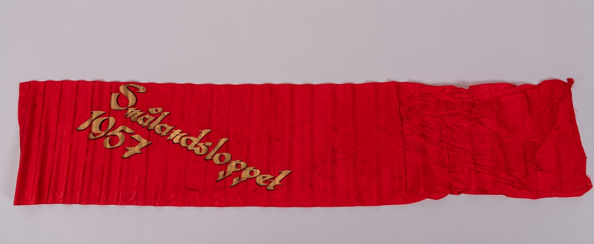 Rött konstsidenband med målad guldtext: "FONALÖBET 1957".