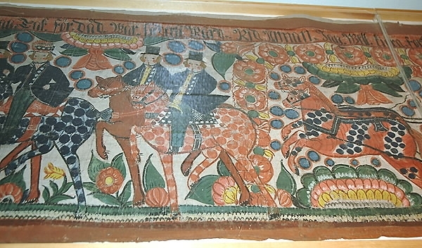 Bröllopsfölje. Bonad målad av Per Svensson. Motiv: Ett bröllopsfölje med feststämning. Bonaden är målad på 1830-talet till en kvinna, JJD. Till vänster är äreporten rest och värdparet välkomnar till bröllopsfesten: "Välkomna gossar, här bestås alla goda drycker efter behag. tack för det vår hederliga värd".Åtta män på hästar rider först. En är brudgummen, en prästen och två spelemän. Sedan kommer bruden i sin vagn: "Rid undan. Jag vill köra fortare, bad bruden. Eller vad tycker ni om vår brud idag. Jo, ganska bra". Sist följer andra bröllopsgäster. Och bruden säger: "Tack för att ni har sett på oss lustigt mina vänner".Kyrkan är längst till höger.