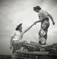 En kvinna hjälper en annan kvinna upp på en vedtrave vid Dön