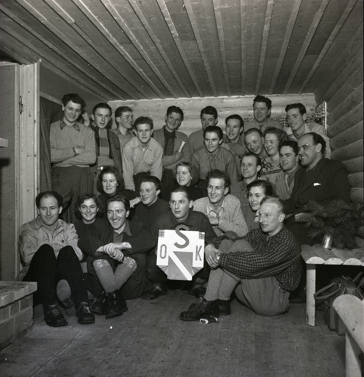 En grupp människor poserar inne i Kallebostugan vid Bocksjön 1950.