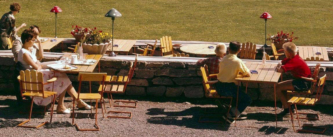 Ett rundt bord med 10 grønnmalte planker som bordplate. Understell av oransjemalt metall. Hull og feste for parasoll.  Stolene er laget av fjærstål som gir mulighet for svikt.