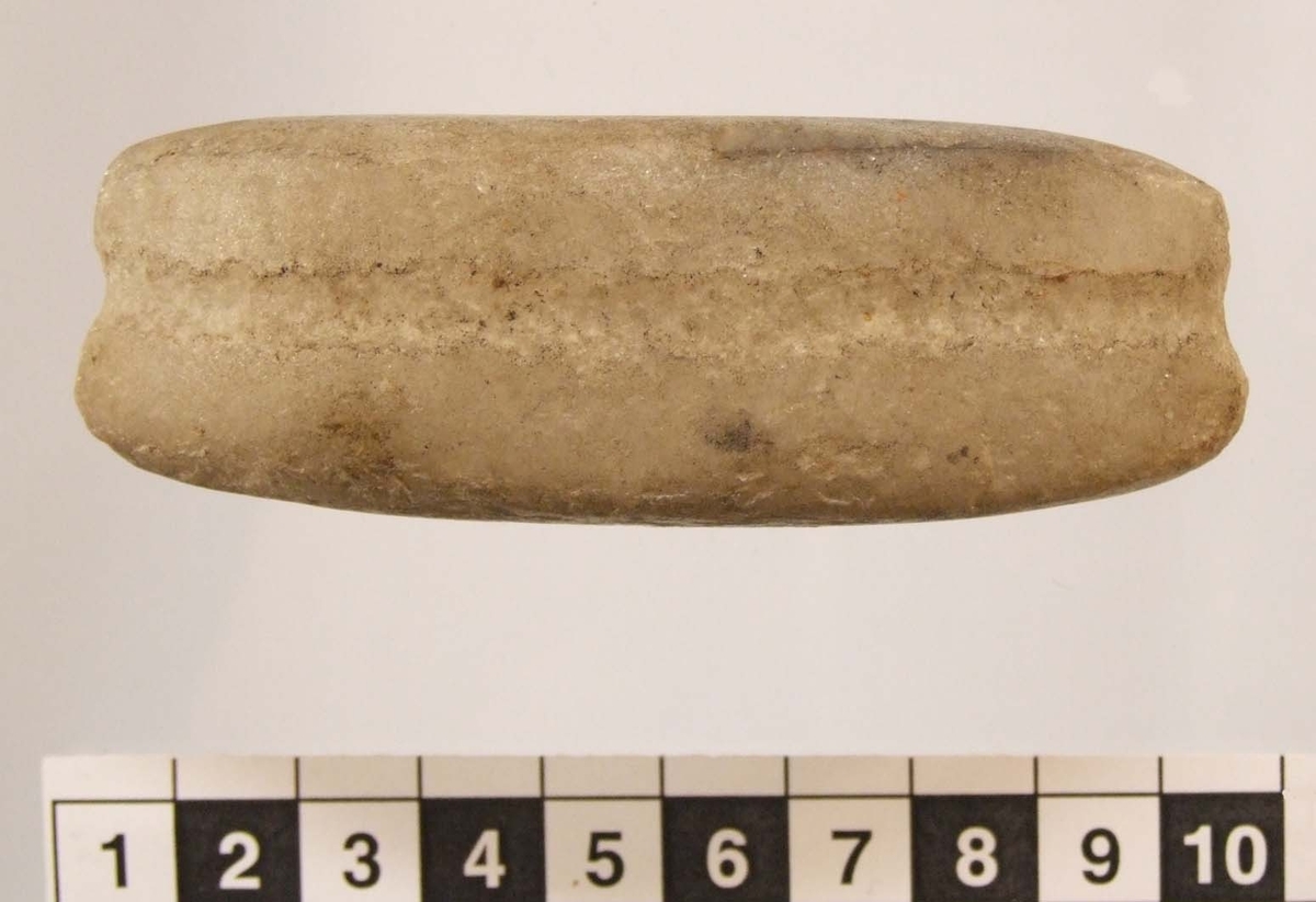 Eldslagningssten  med spetsoval form, ena flatsidan något konvex. Grund smal ränna runt om, 5 mm br och 0,5 mm dj. Antydan till slagspår på ena flatsidan.