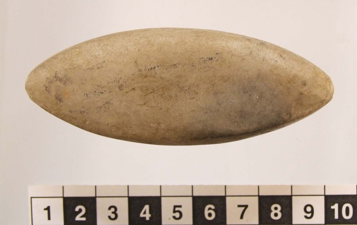 Eldslagningssten  med spetsoval form, ena flatsidan något konvex. Grund smal ränna runt om, 5 mm br och 0,5 mm dj. Antydan till slagspår på ena flatsidan.