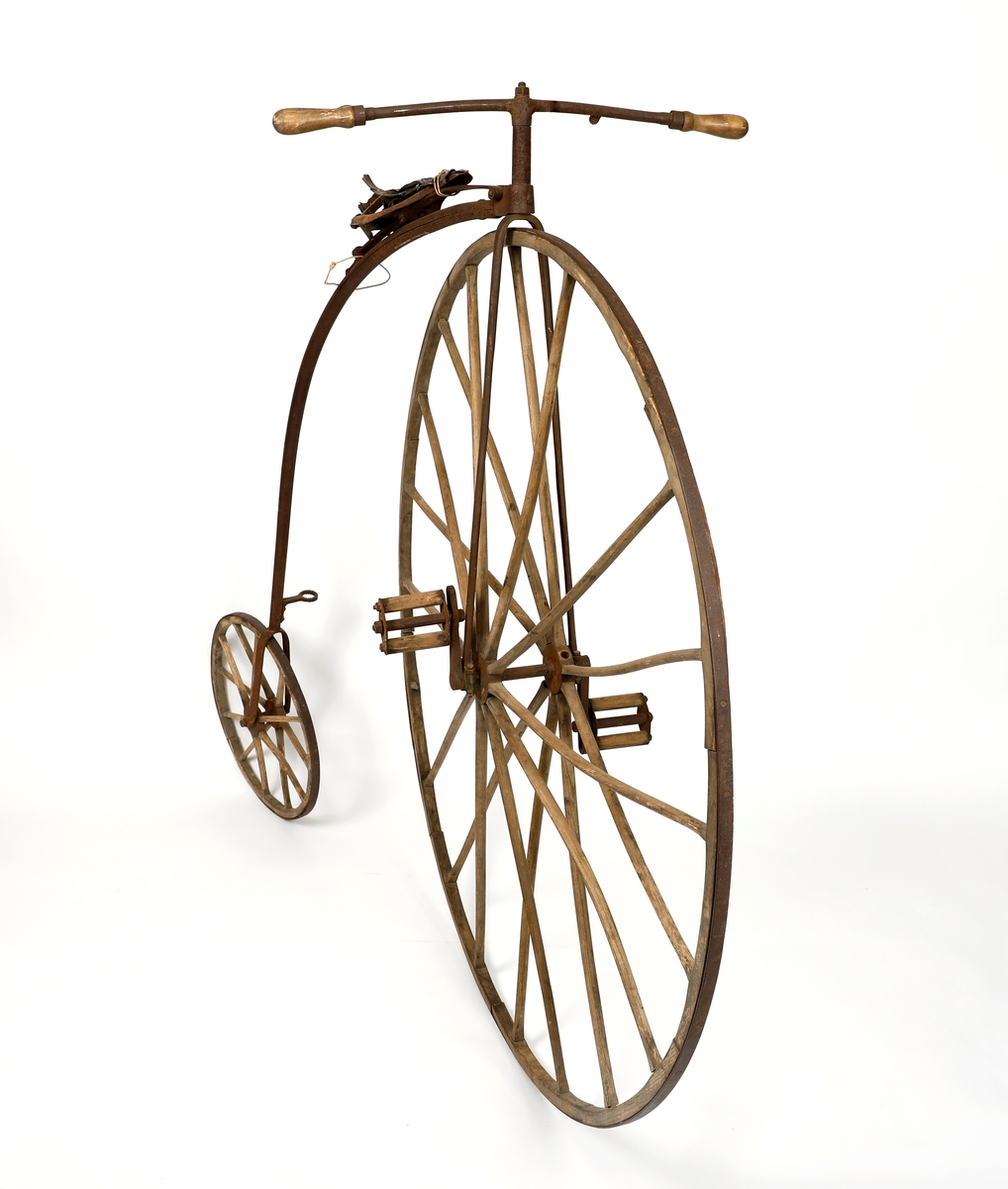 Veltepetter i med hjul av tre og stang av metall. Justerbart sete og pedaler. Sete trukket i lær. Styreholker av tre.