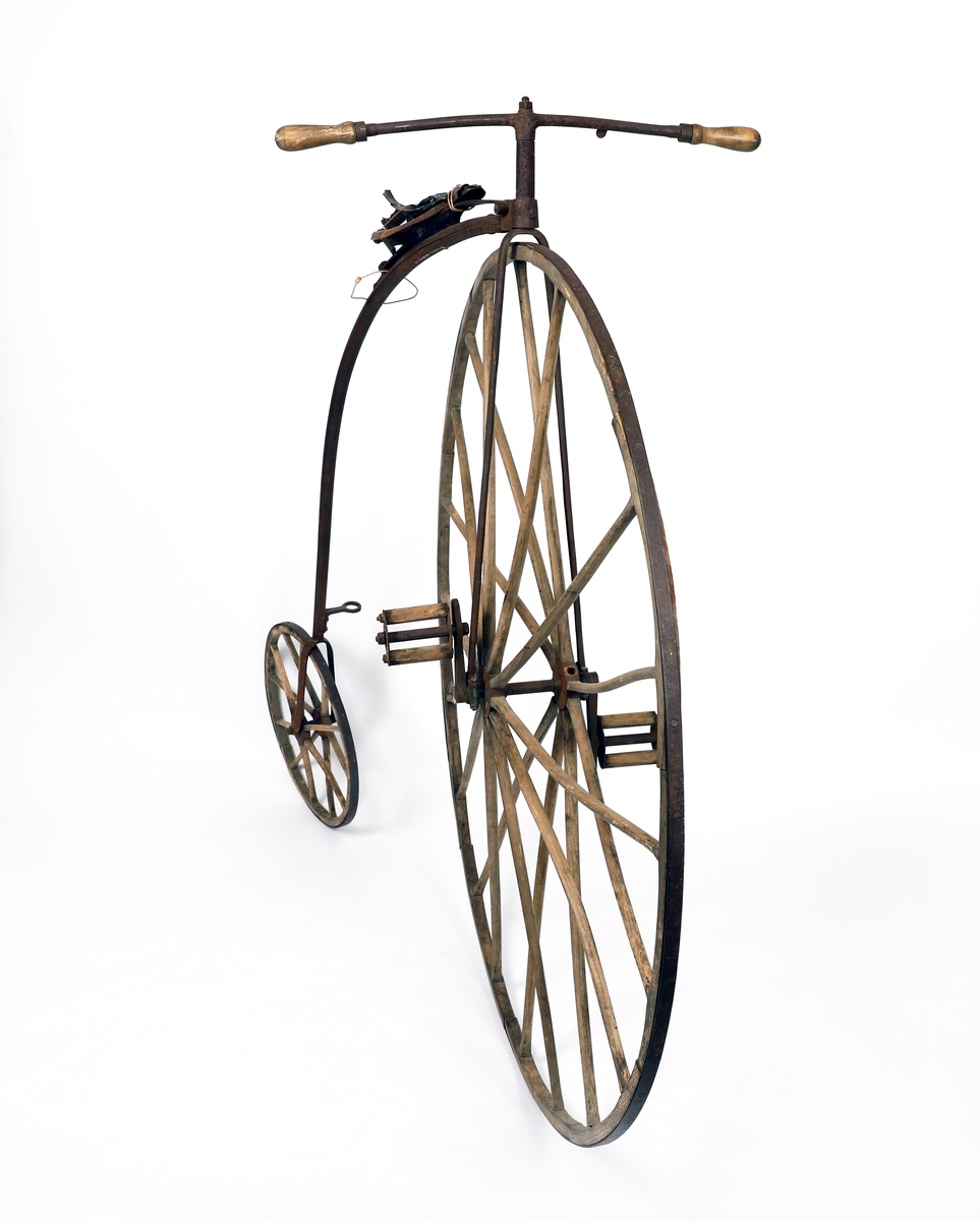Veltepetter i med hjul av tre og stang av metall. Justerbart sete og pedaler. Sete trukket i lær. Styreholker av tre.