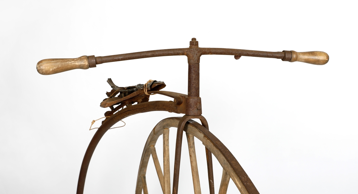 Veltepetter i med hjul av tre og stang av metall. Justerbart sete og pedaler. Sete trukket i lær. Styreholker av tre.