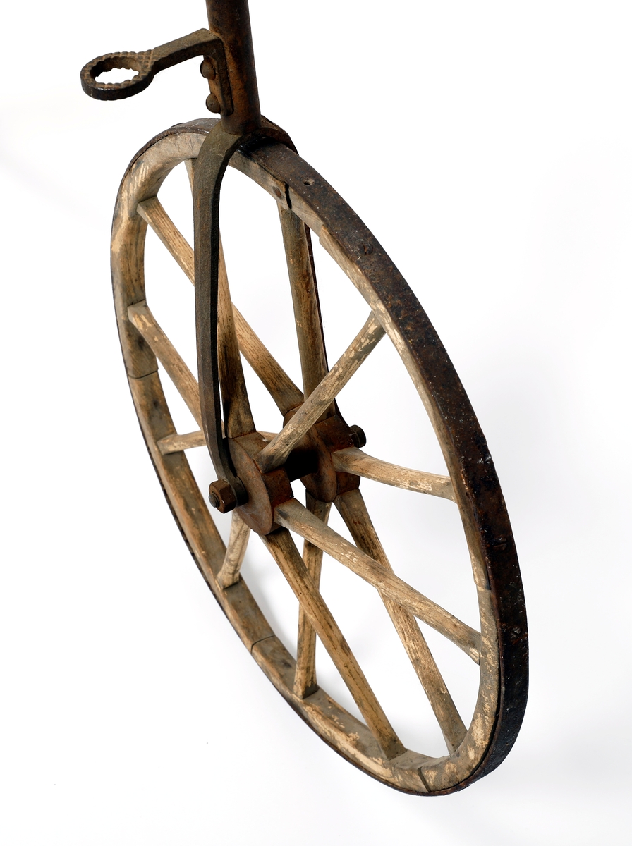 Veltepetter i med hjul av tre og stang av metall. Justerbart sete og pedaler. Sete trukket i lær. Styreholker av tre.