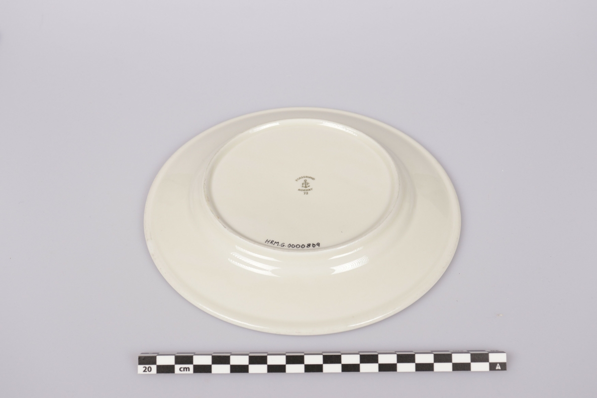 3mm gullfarget stripe langs ytterkant. Rederiflagget til Det Bergenske Dampskibselskab er trykt på kanten av asjetten. På indrekanten er trykt en 1mm gullfarget stripe, som har blitt svak på noen steder. 