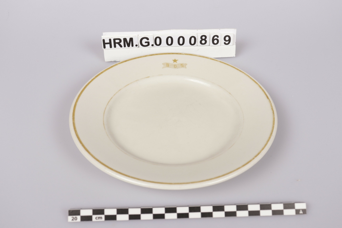 3mm gullfarget stripe langs ytterkant. Rederiflagget til Det Bergenske Dampskibselskab er trykt på kanten av asjetten. På indrekanten er trykt en 1mm gullfarget stripe, som har blitt svak på noen steder. 