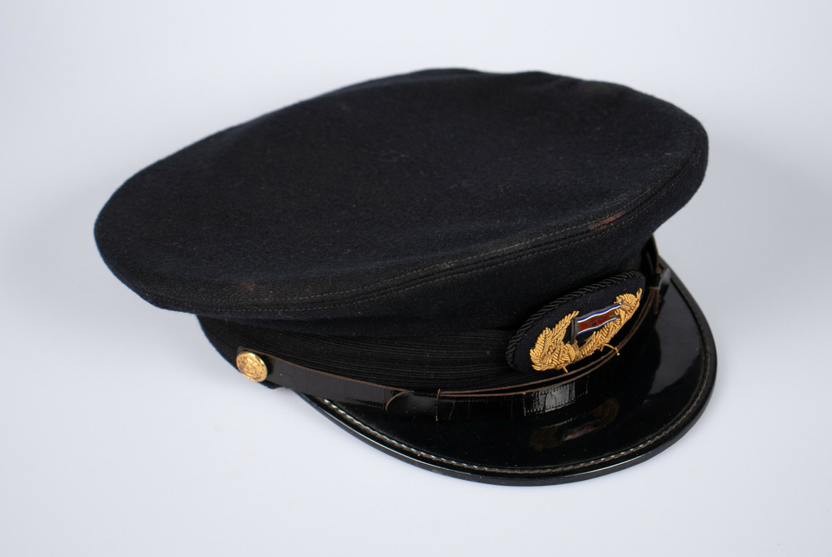 Svart uniformslue med skjerm og rederiflagg på luemerke. To gullfargede knapper i hver side av skjermen  med et svart bånd mellom. Gjennomsiktig plastikk hette er tredd over pullen.