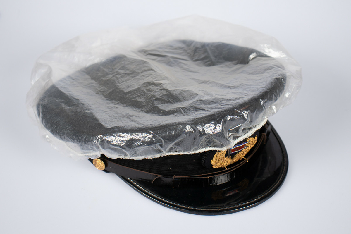 Svart uniformslue med skjerm og rederiflagg på luemerke. To gullfargede knapper i hver side av skjermen  med et svart bånd mellom. Gjennomsiktig plastikk hette er tredd over pullen.