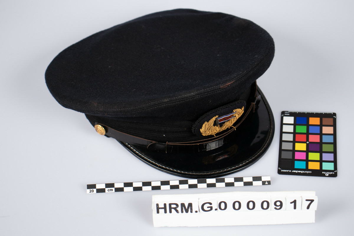Svart uniformslue med skjerm og rederiflagg på luemerke. To gullfargede knapper i hver side av skjermen  med et svart bånd mellom. Gjennomsiktig plastikk hette er tredd over pullen.
