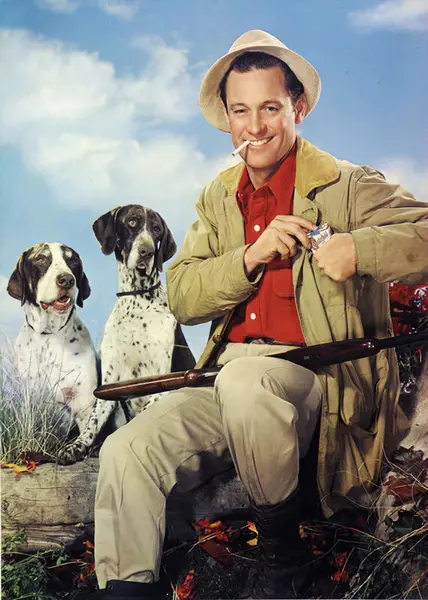 Motivet viser en mann som sitter og røyker. Han har to hunder sittende ved siden av seg.