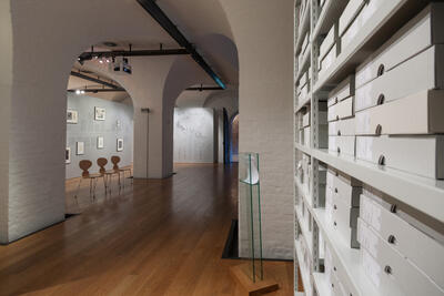 Dokumentasjonsbilde fra utstillingsrommet. Tekst og bilder på vegg og en hylle med arkivmateriale.